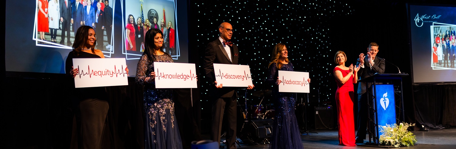 Six people standing on stage holding up signs reading equity, knowledge, discovery, and advocacy.